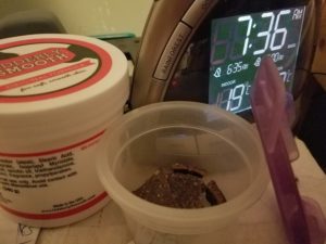 open plastic container of dog treats next to alarm clock and hand cream